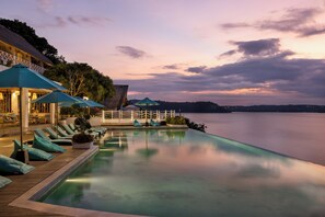 A serene infinity pool with lounge chairs and umbrellas, overlooking a calm body of water at dusk. - Pramana Natura Nusa Penida (Penida Island)