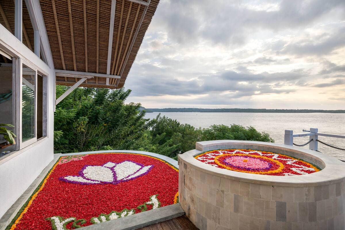 Un balcón con vista al mar, un arreglo floral y un edificio con techo de paja.