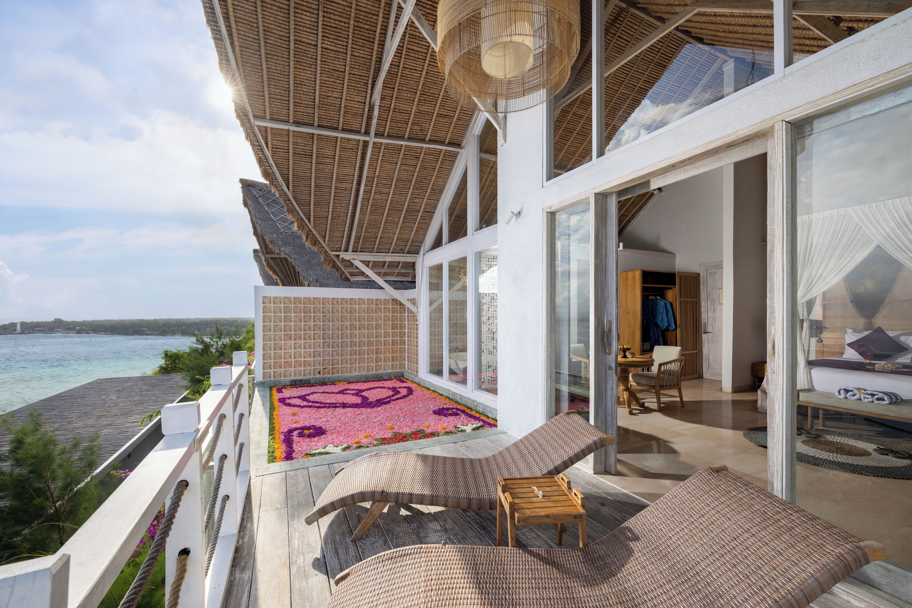 A balcony with a view of the sea, a lounge chair, a small table, and a glass door leading to a room.