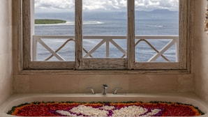 Un baño con bañera, ventana con vista al océano y un arreglo floral decorativo.