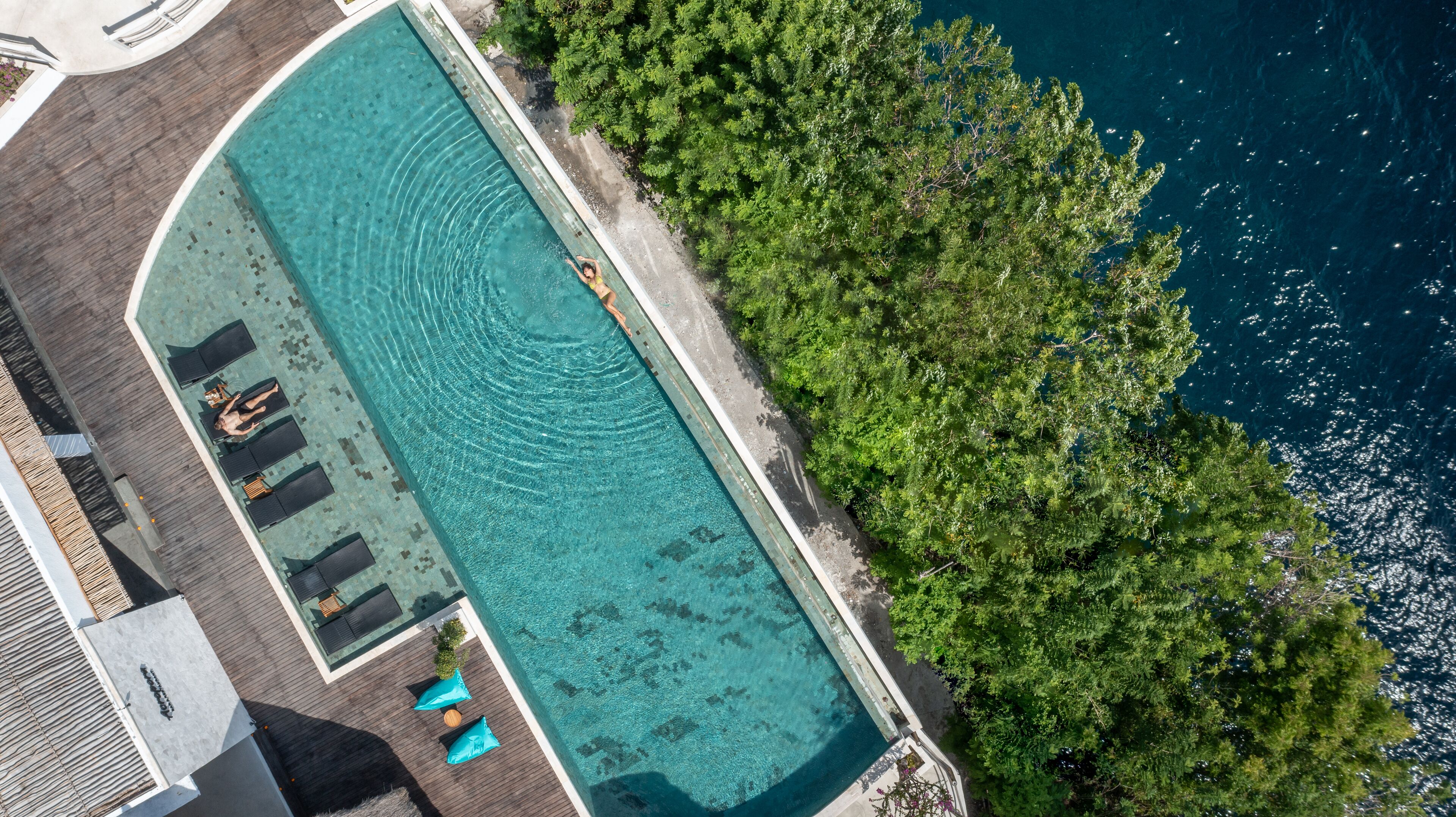 Vue aérienne d’une piscine rectangulaire à l’eau claire, entourée d’une terrasse en bois et de chaises longues.