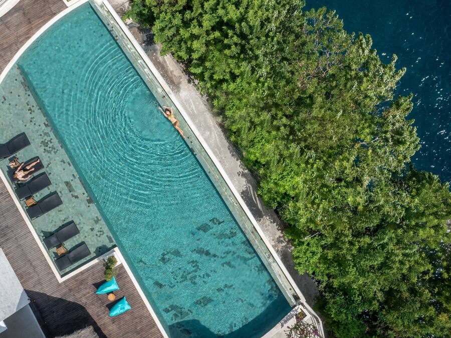 An aerial view of a rectangular swimming pool with clear water, surrounded by a wooden deck and lounge chairs.