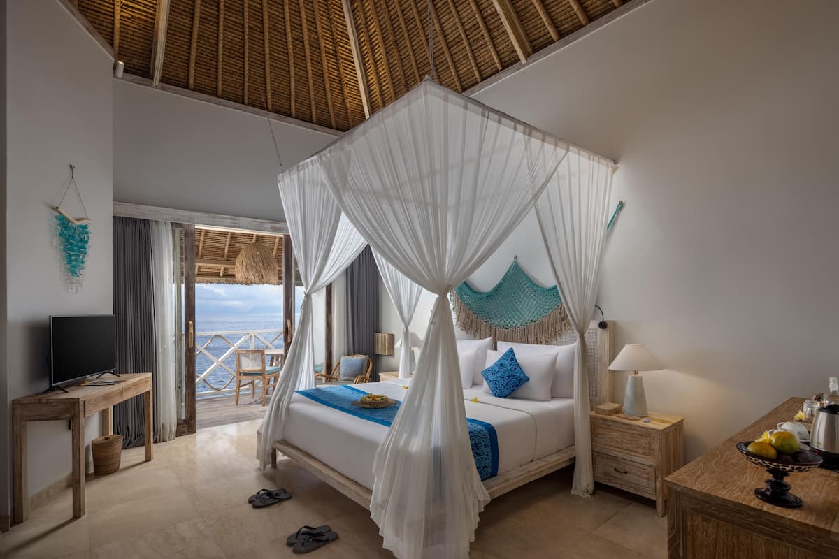Un dormitorio con cama con dosel, televisión, mesita de noche y vista al mar.