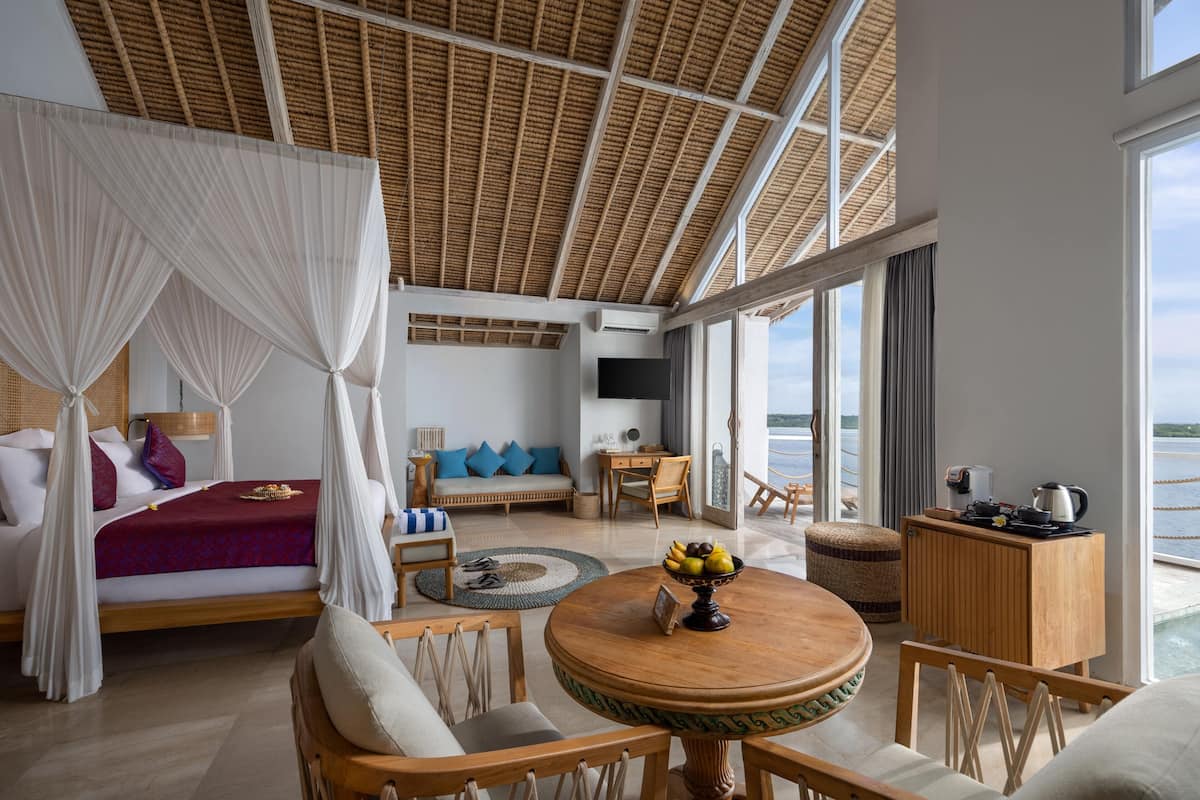 Una habitación amplia con una cama, una mesa redonda de madera con frutero, un sofá y un televisor.