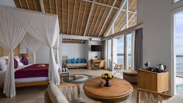 Una habitación amplia con una cama, una mesa redonda de madera con frutero, un sofá y un televisor.