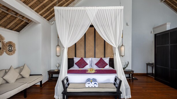 Quarto com cama de dossel, sofá e mesa de cabeceira com abajur.