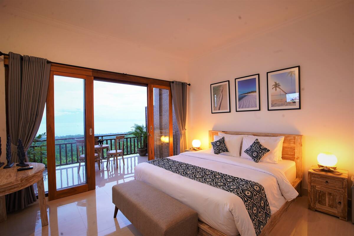 A bedroom with a large bed, a balcony, and three framed pictures on the wall.