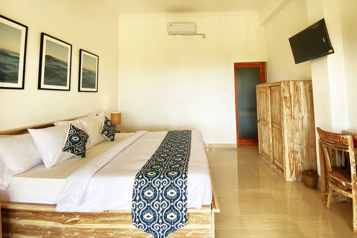 A hotel room with a bed, a television mounted on the wall, and a wooden wardrobe.