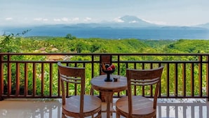 A balcony with two wooden chairs and a small round table, overlooking a lush green landscape and a distant view of the sea and mountains. - Mere Sea View Penida (Penida Island)