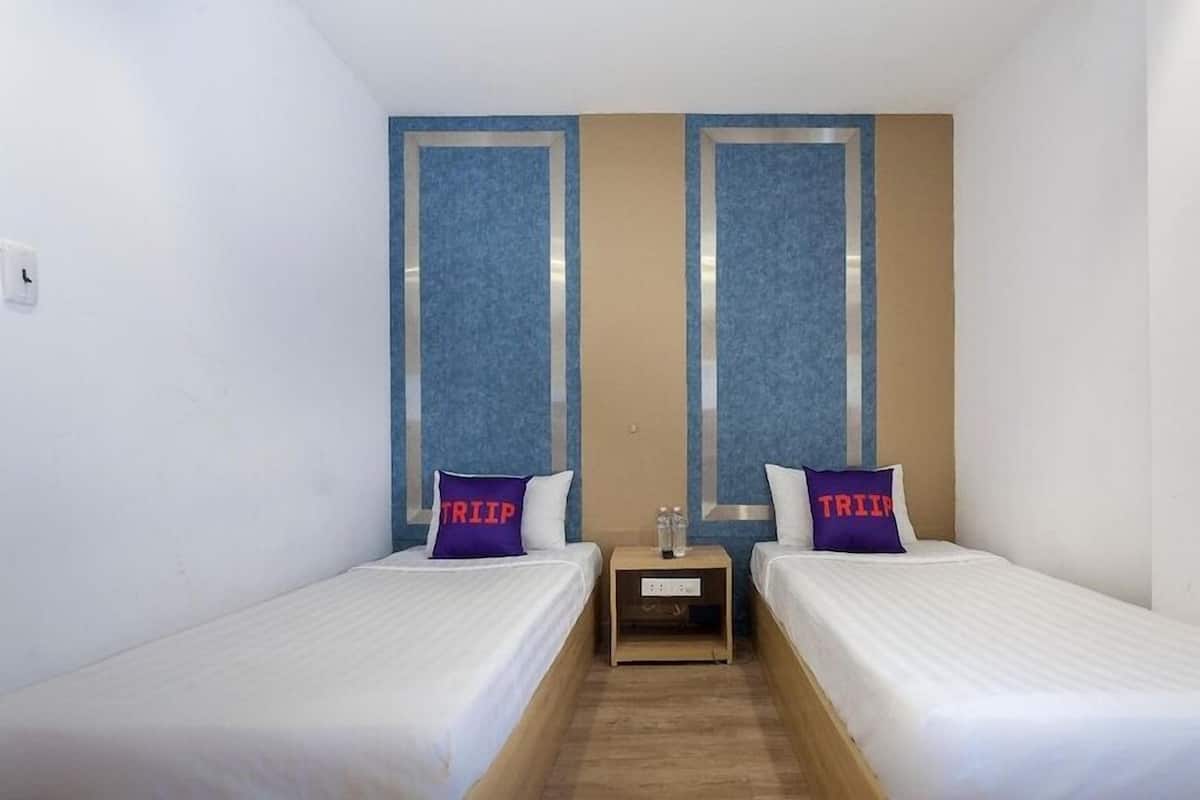 A small, clean room with two single beds, a wooden nightstand, and a wall-mounted shelf.