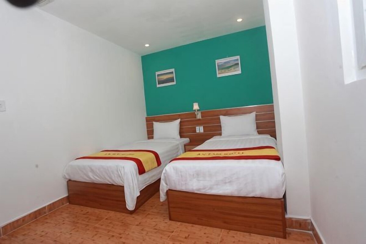 Une chambre avec deux lits, des têtes de lit en bois, du linge de lit blanc et un mur d’accent de couleur turquoise.