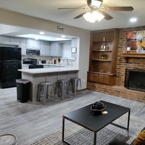 A modern kitchen with grey cabinets, a black refrigerator, and a central island with stools. - Chisholm Comfort (Oklahoma City)