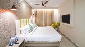 A hotel room with a bed, a TV, a ceiling fan, and a nightstand with a remote control and water bottles. - The Beacon Hotel Visakhapatnam (Visakhapatnam)