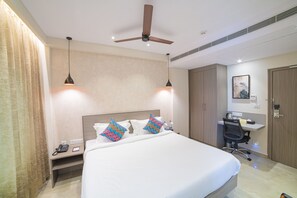 A hotel room with a bed, bedside table, desk, chair, and a ceiling fan. - The Beacon Hotel Visakhapatnam (Visakhapatnam)