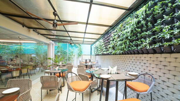 An outdoor patio area with wicker furniture, orange cushions, and a brick wall with green plants. - The Beacon Hotel Visakhapatnam (Visakhapatnam)