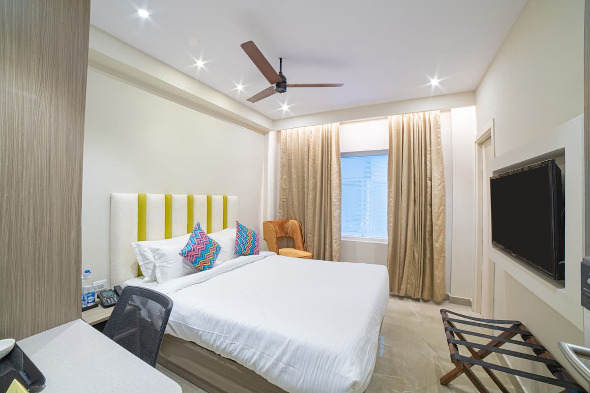 A hotel room with a bed, a desk, a chair, a television, and a ceiling fan.
