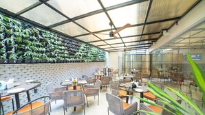 A covered outdoor seating area with wicker chairs and tables, surrounded by potted plants. - The Beacon Hotel Visakhapatnam (Visakhapatnam)