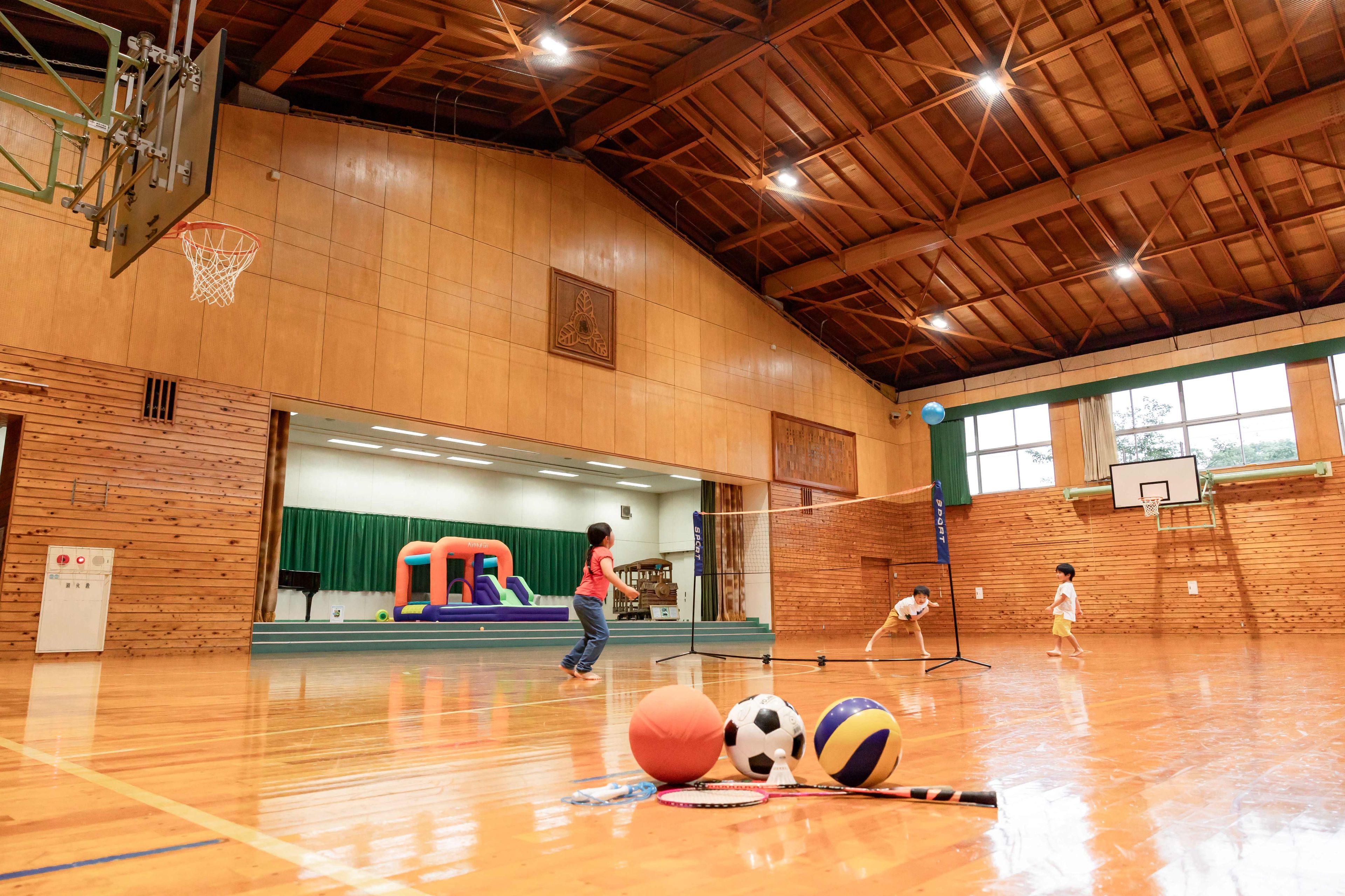 An indoor sports facility with a basketball court, a volleyball net, and a climbing wall.