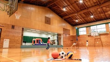 An indoor sports facility with a basketball court, a volleyball net, and a climbing wall.