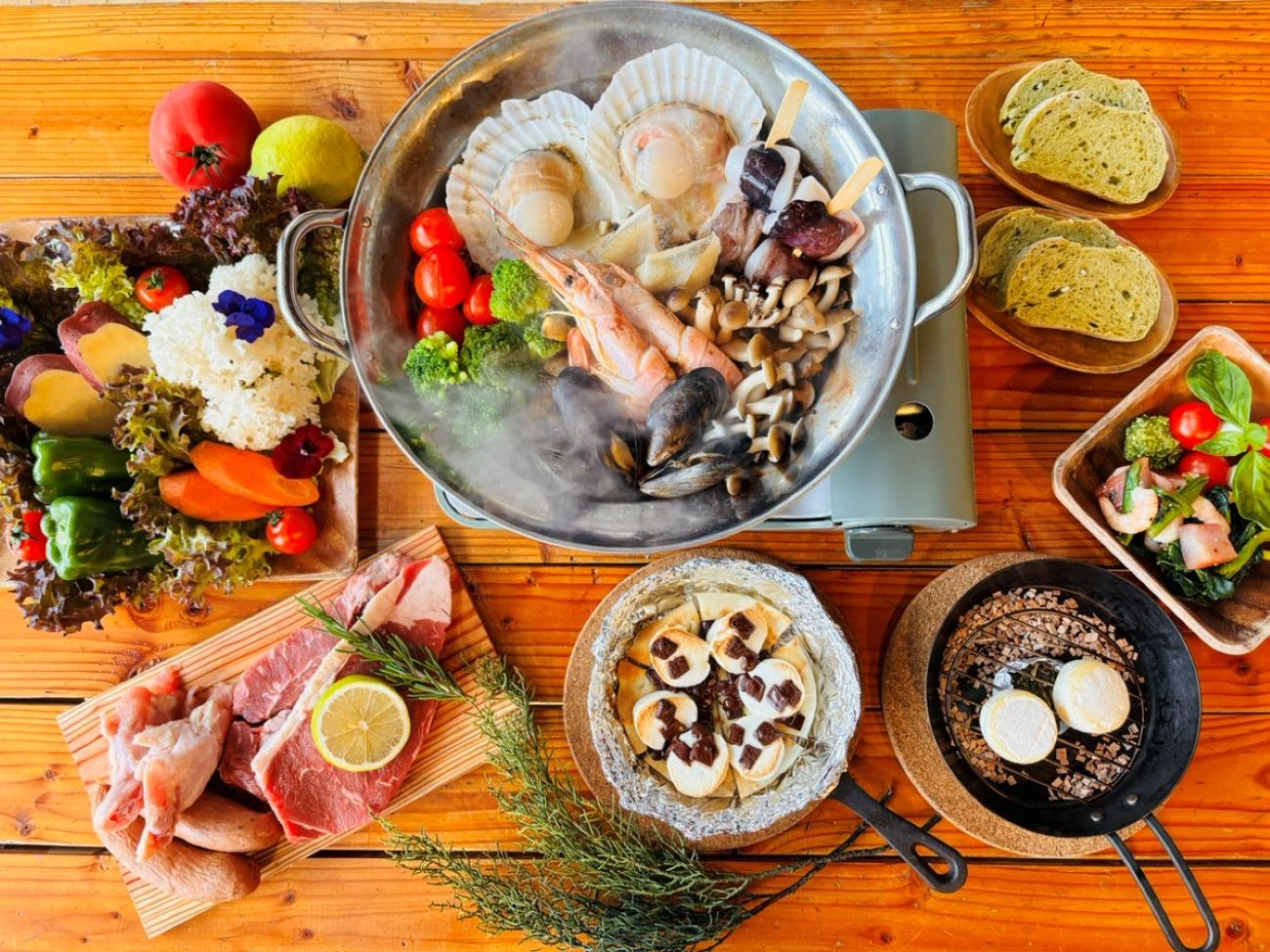 A variety of seafood and meats on a wooden table, including scallops, shrimp, and a pan with seafood.