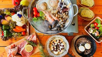 A variety of seafood and meats on a wooden table, including scallops, shrimp, and a pan with seafood.