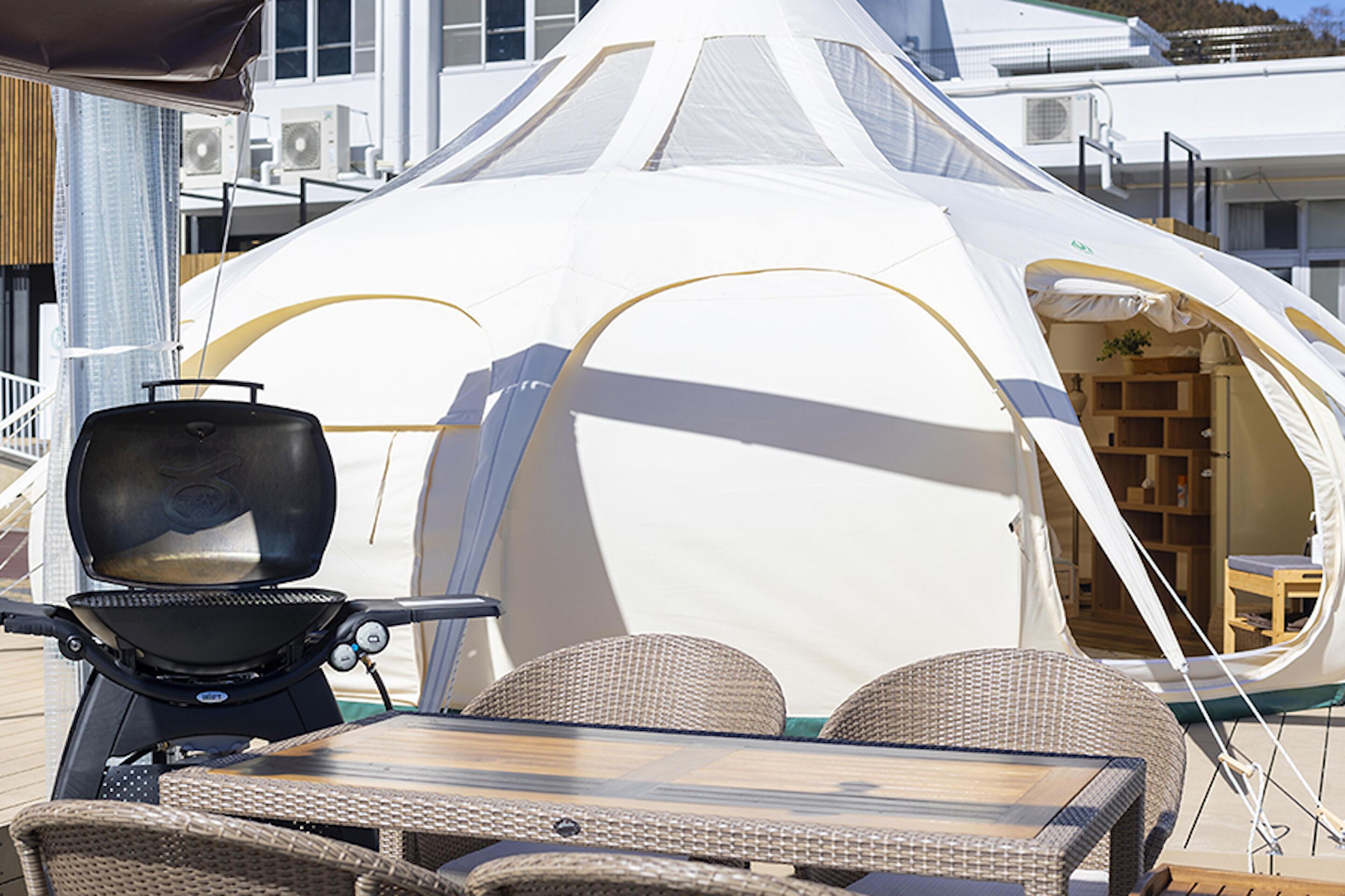 A white tent with a grill and wicker furniture outside.