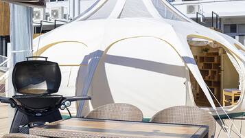 A white tent with a grill and wicker furniture outside.