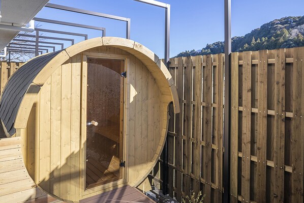 A wooden sauna with a curved roof, a door, and a wooden deck. - Glamping & Port (Shimada)
