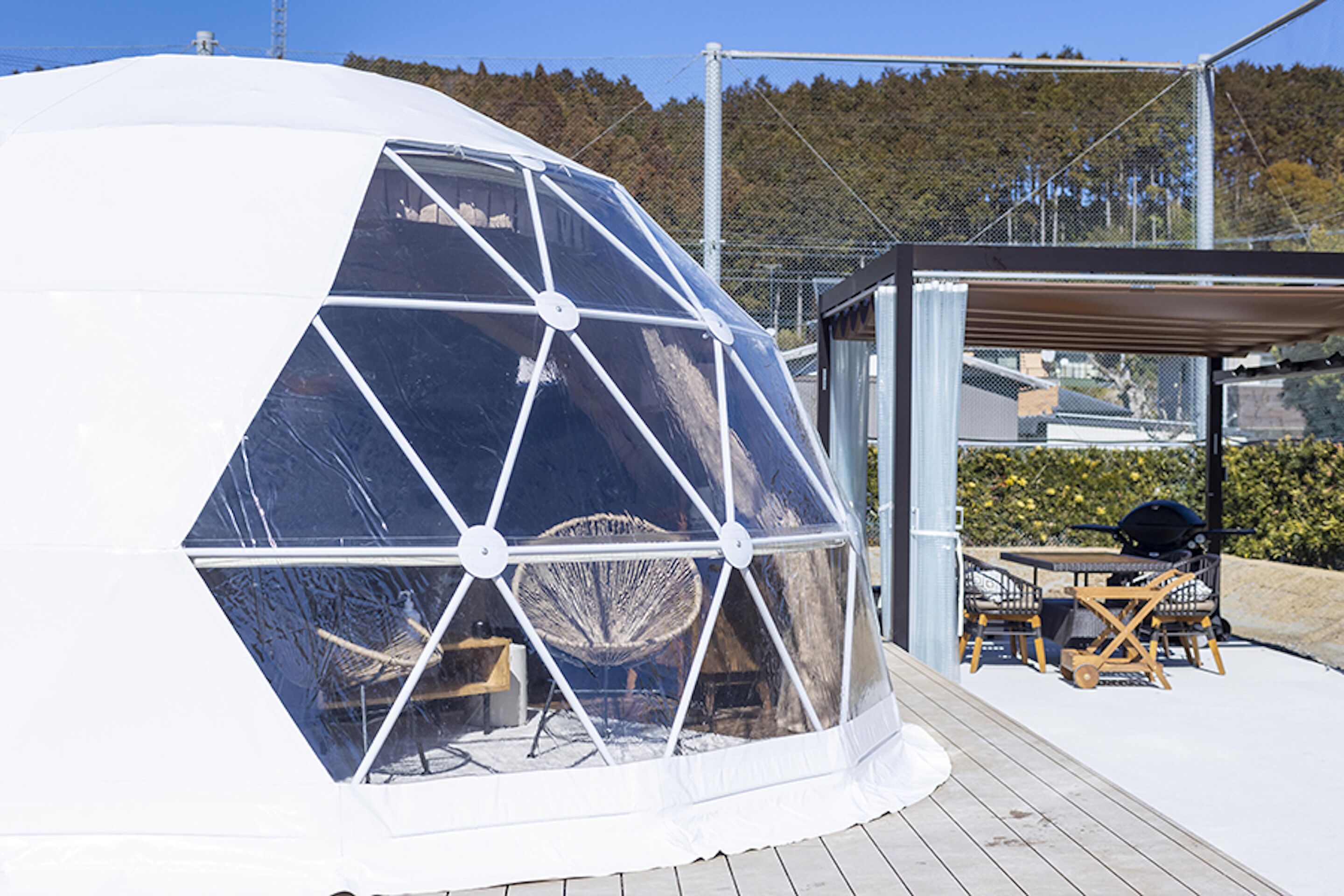 A geodesic dome structure with a transparent window, a wooden deck, and outdoor furniture.