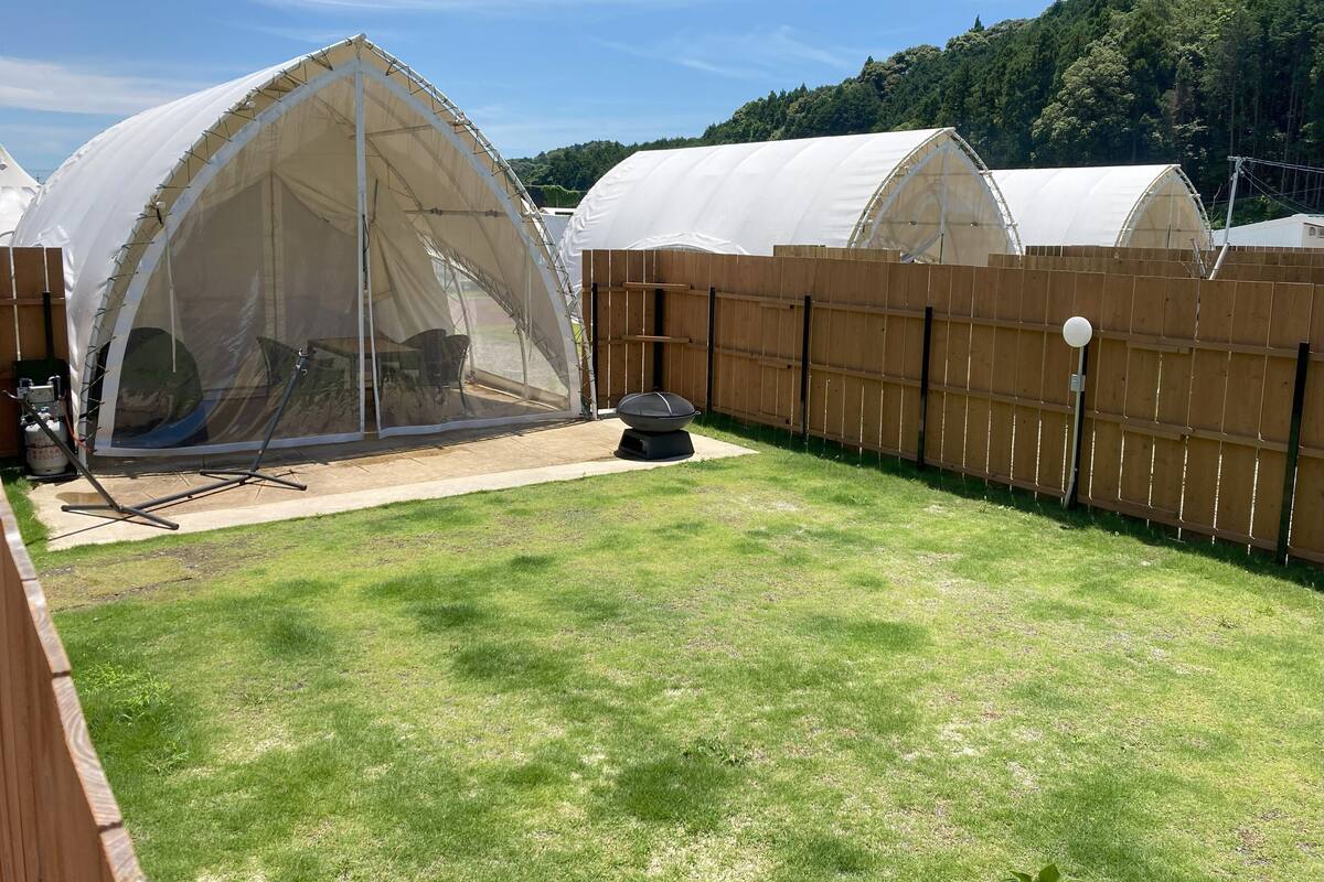 A backyard with a large tent-like structure, a wooden fence, and a grassy lawn.