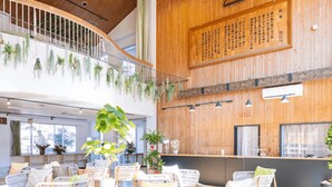 A spacious indoor area with wicker furniture, wooden walls, and hanging plants. - Glamping & Port (Shimada)