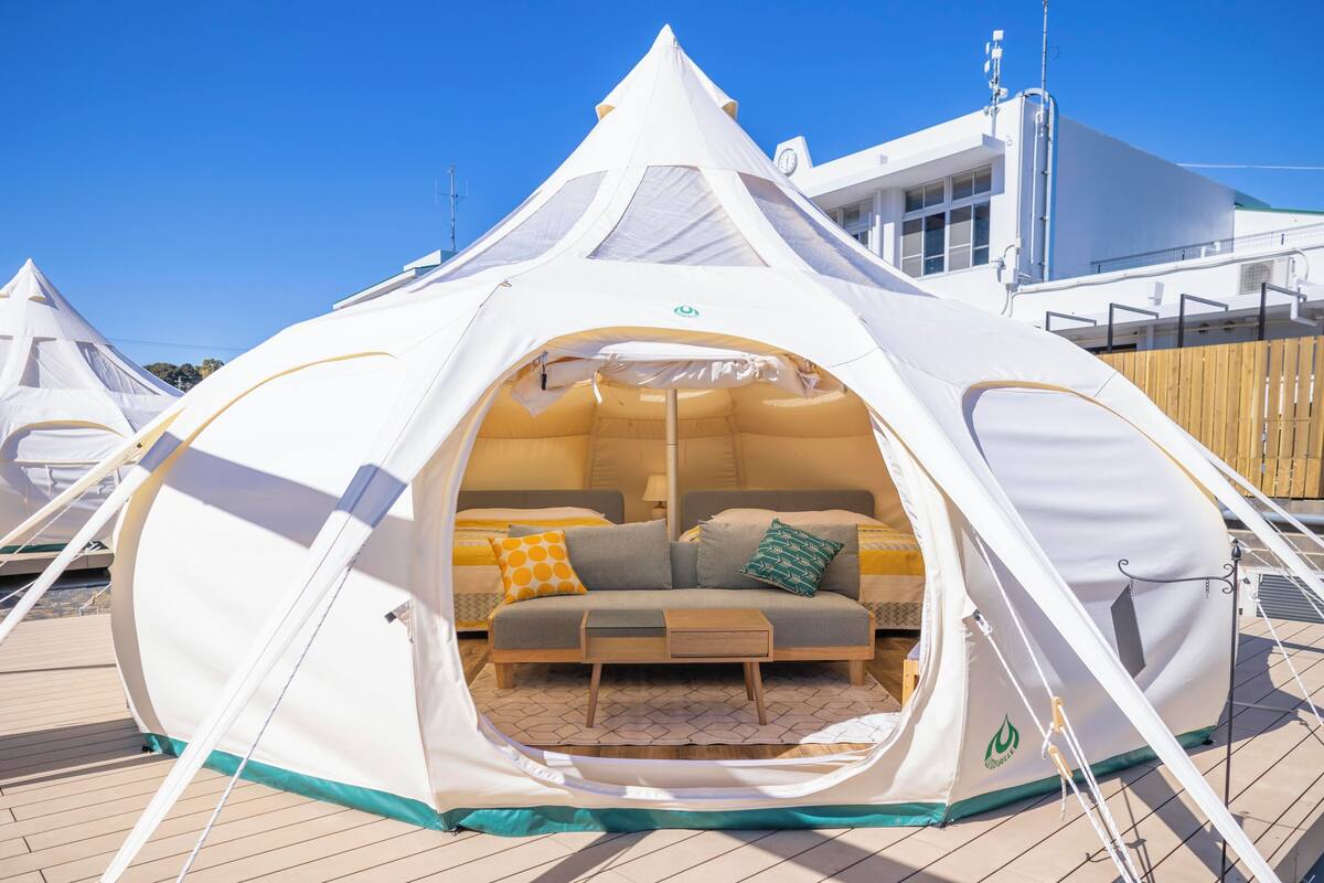A dome-shaped tent with a bed and a small table inside, set on a wooden deck.