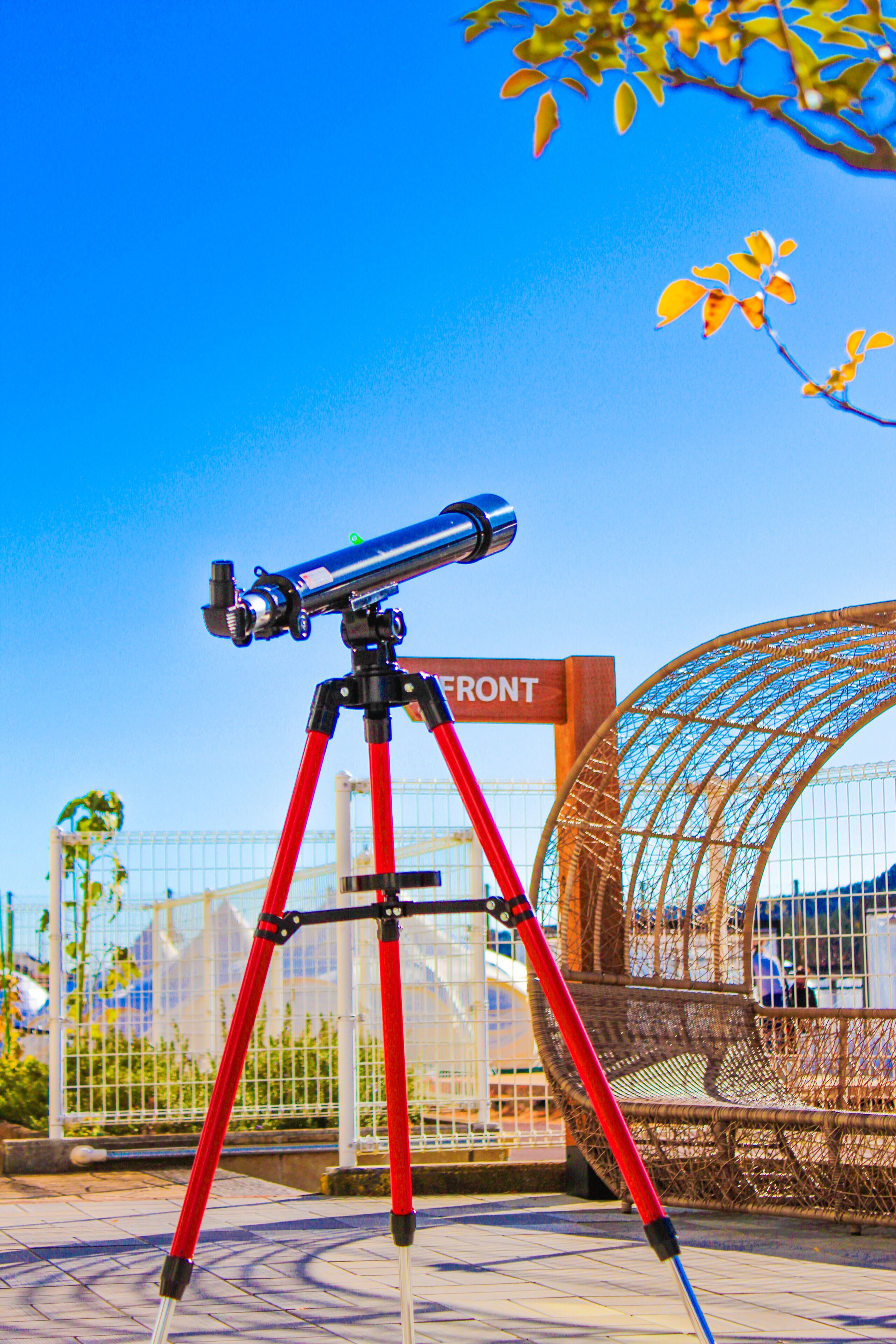 A telescope on a red tripod in an outdoor area with a sign that reads "FRONT".