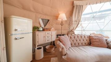 Um quarto tipo tenda aconchegante, com uma geladeira de estilo antigo, um sofá estofado, uma luminária e uma janela com cortinas.