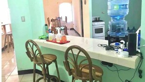 A kitchen with a bar area, two wooden chairs, a water dispenser, and various kitchen appliances.