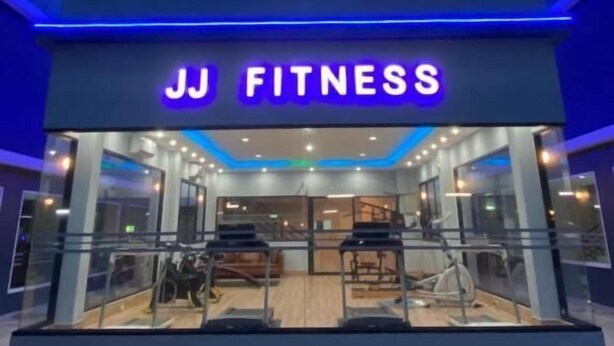 Ein Fitnessstudio mit einer Neonreklame mit dem Schriftzug "JJ FITNESS" und einem Glastür-Eingang.