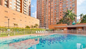 Une piscine dotée d’une terrasse carrelée, entourée d’une clôture et de palmiers.