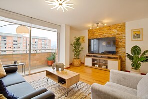 A modern living room with a sofa, TV, and potted plants. - Nomad's Dream Condo el Poblado 300MBS, Pool, Gym (Medellín)