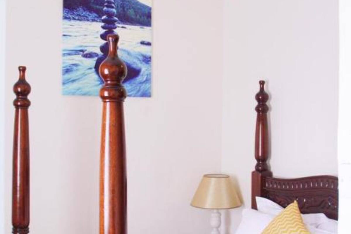 A four-poster bed with a wooden headboard, a beige throw blanket, and a yellow pillow.