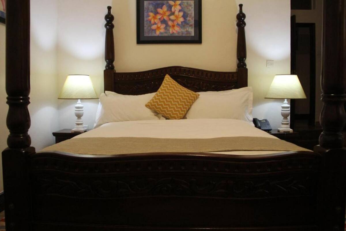 A four-poster bed with a wooden headboard, two bedside lamps, and a framed floral artwork on the wall.