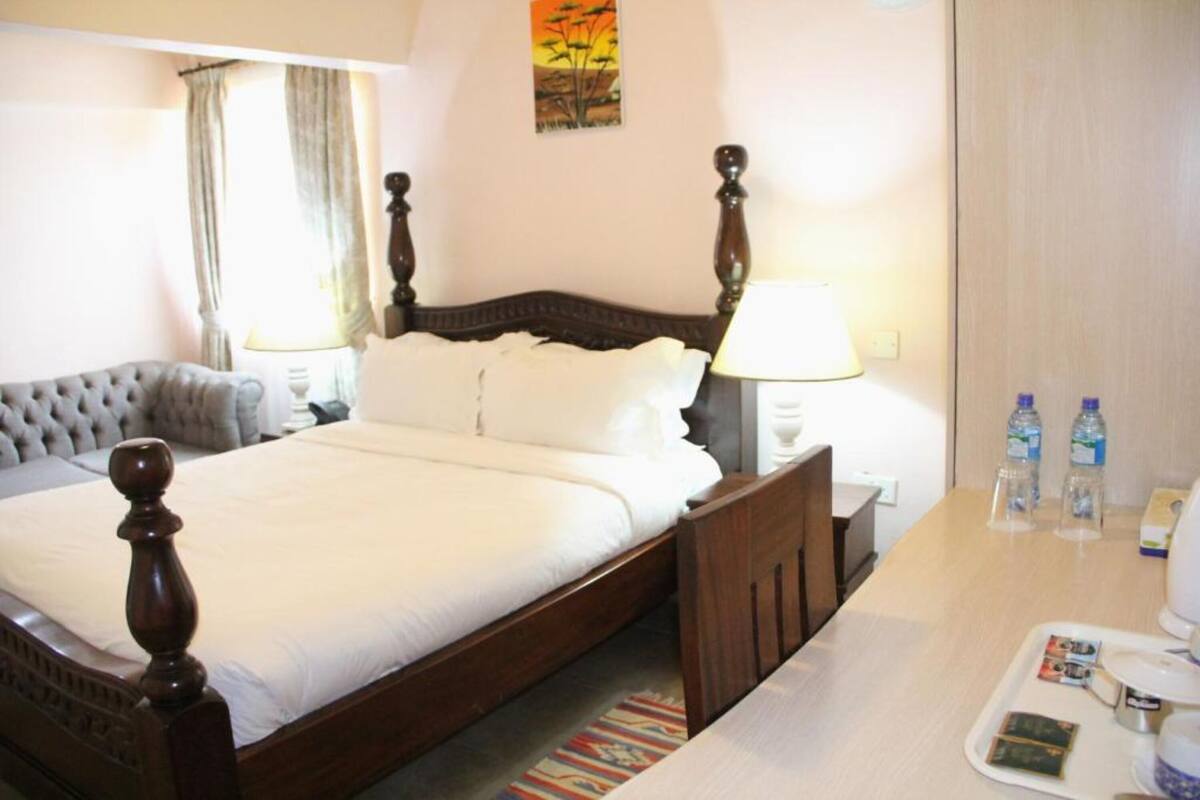 A hotel room with a bed, bedside table, lamp, and a painting on the wall.