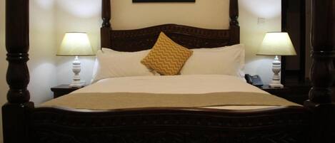 Una cama con dosel, cabecera de madera, dos lámparas de noche, un cojín decorativo y una obra de arte floral enmarcada en la pared.