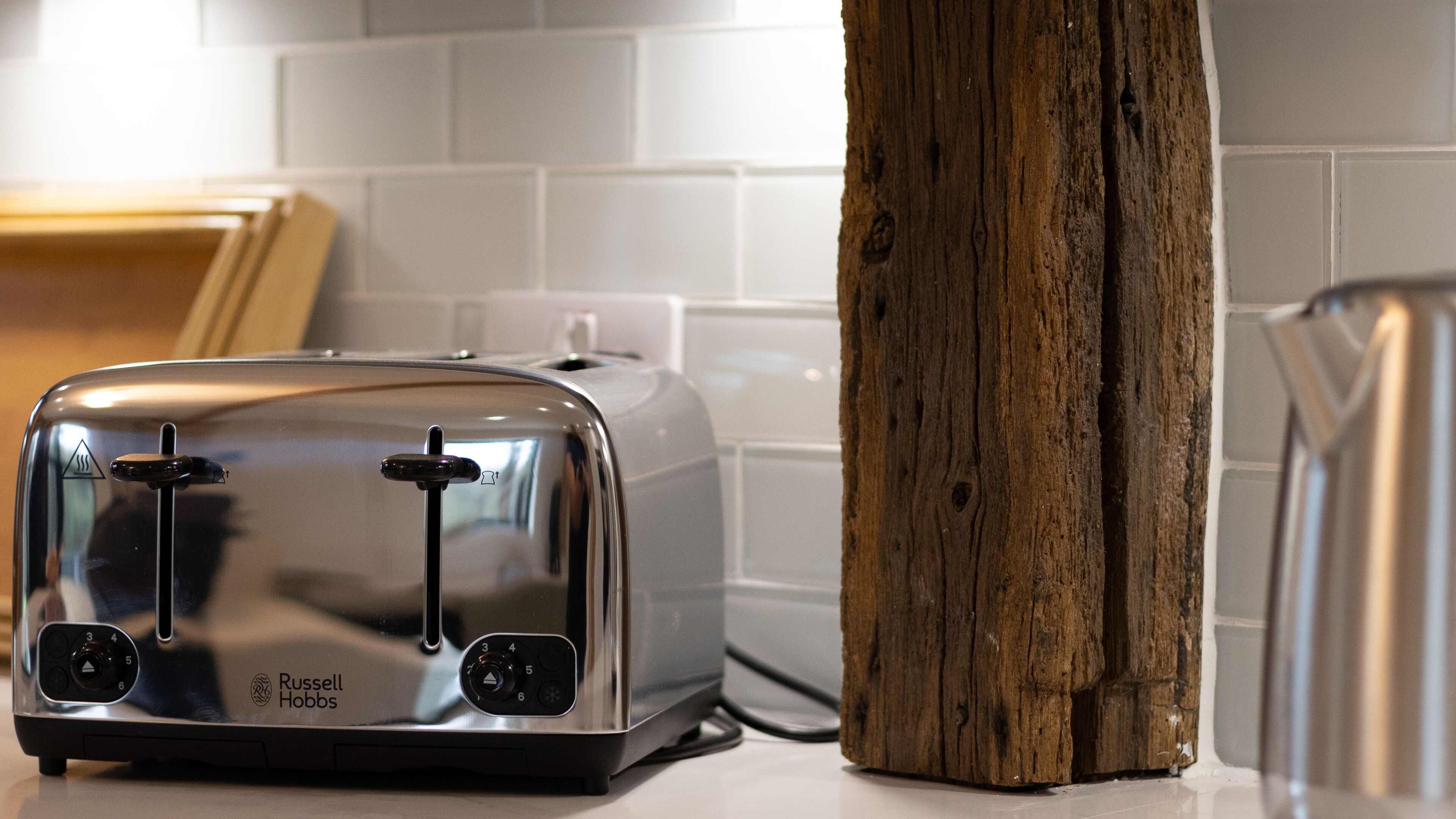 Een moderne keuken met een RVS-toaster op een aanrecht, een houten snijplank en een witte betegelde spatwand.