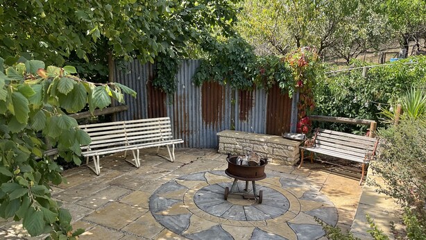 A patio with stone flooring, two wooden benches, and a central fire pit. - Family farm retreat, big outdoor alfresco areas, with emus (Barwidgee)