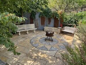 Eine Terrasse mit Steinbelag, zwei hölzernen Bänken und einem Feuerkorb in der Mitte.