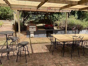 An outdoor patio with a brick floor, a wooden table, metal chairs, a barbecue grill, and a built-in oven. - Family farm retreat, big outdoor alfresco areas, with emus (Barwidgee)