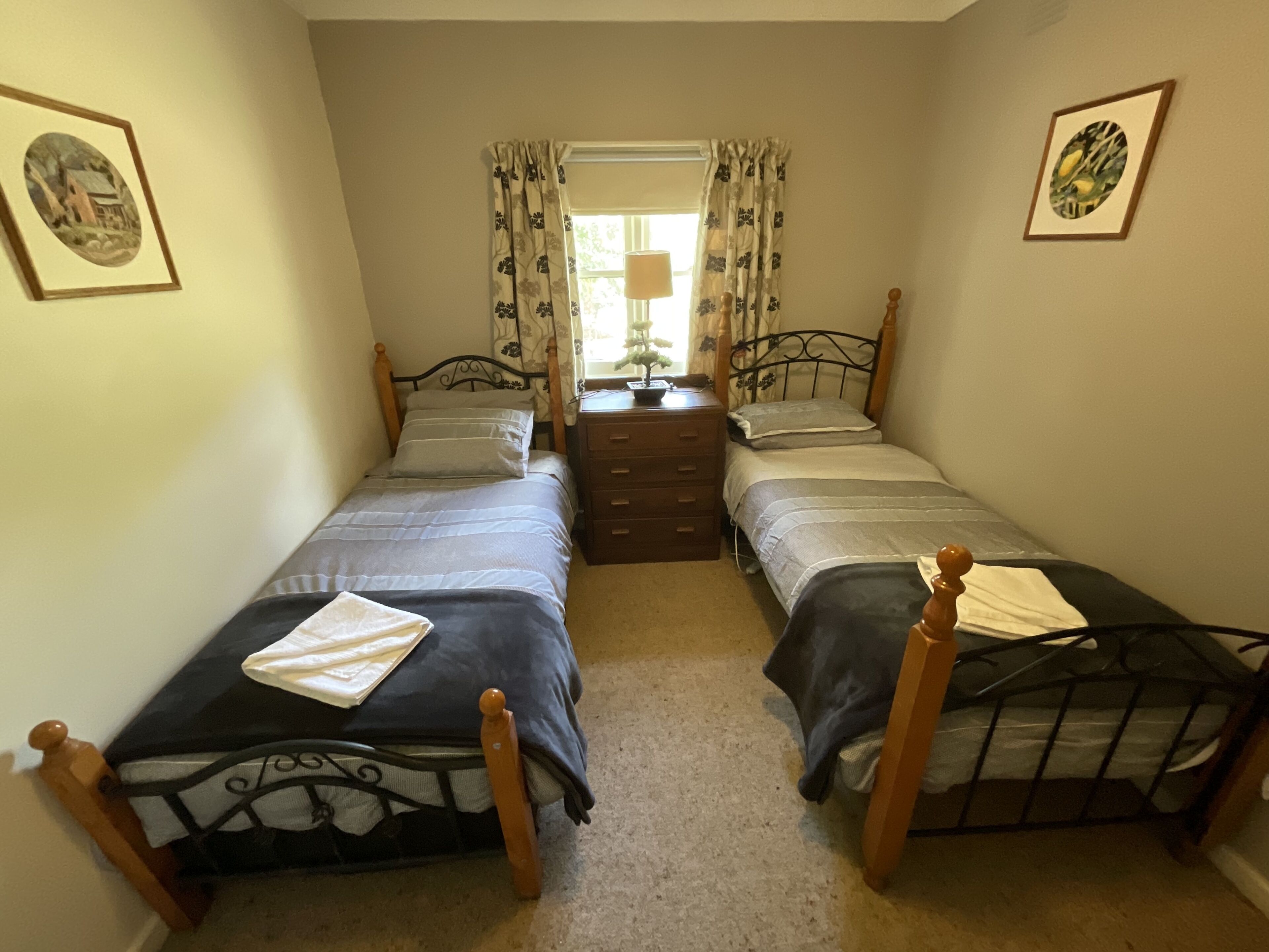 A bedroom with two single beds, a dresser, and a window with curtains.