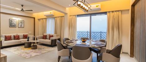 Una sala de estar moderna con comedor, un conjunto de sofás, una mesa de centro y vista al mar a través de amplios ventanales.