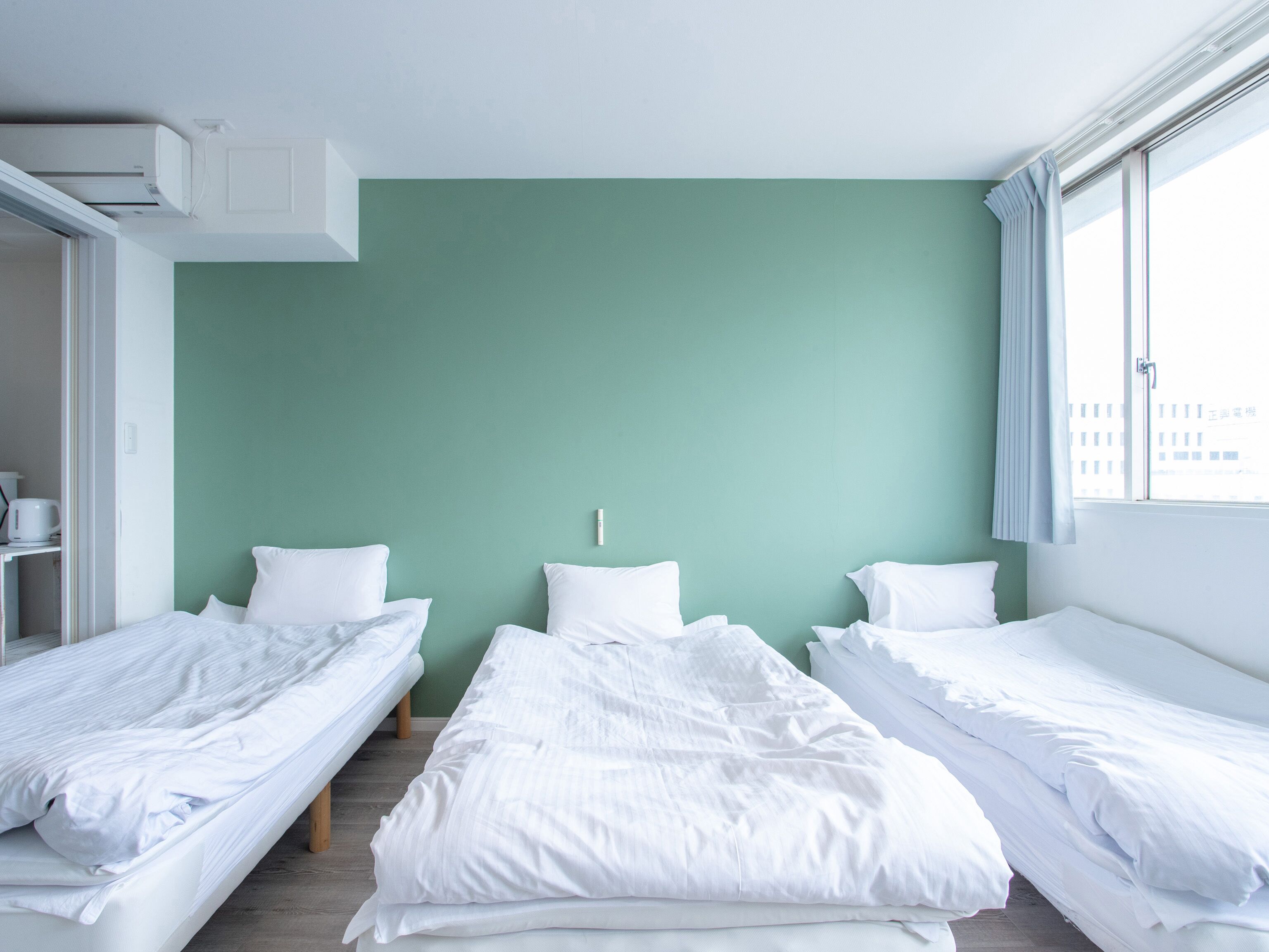 Habitación de hotel con dos camas individuales, una pared verde y una ventana con cortinas.