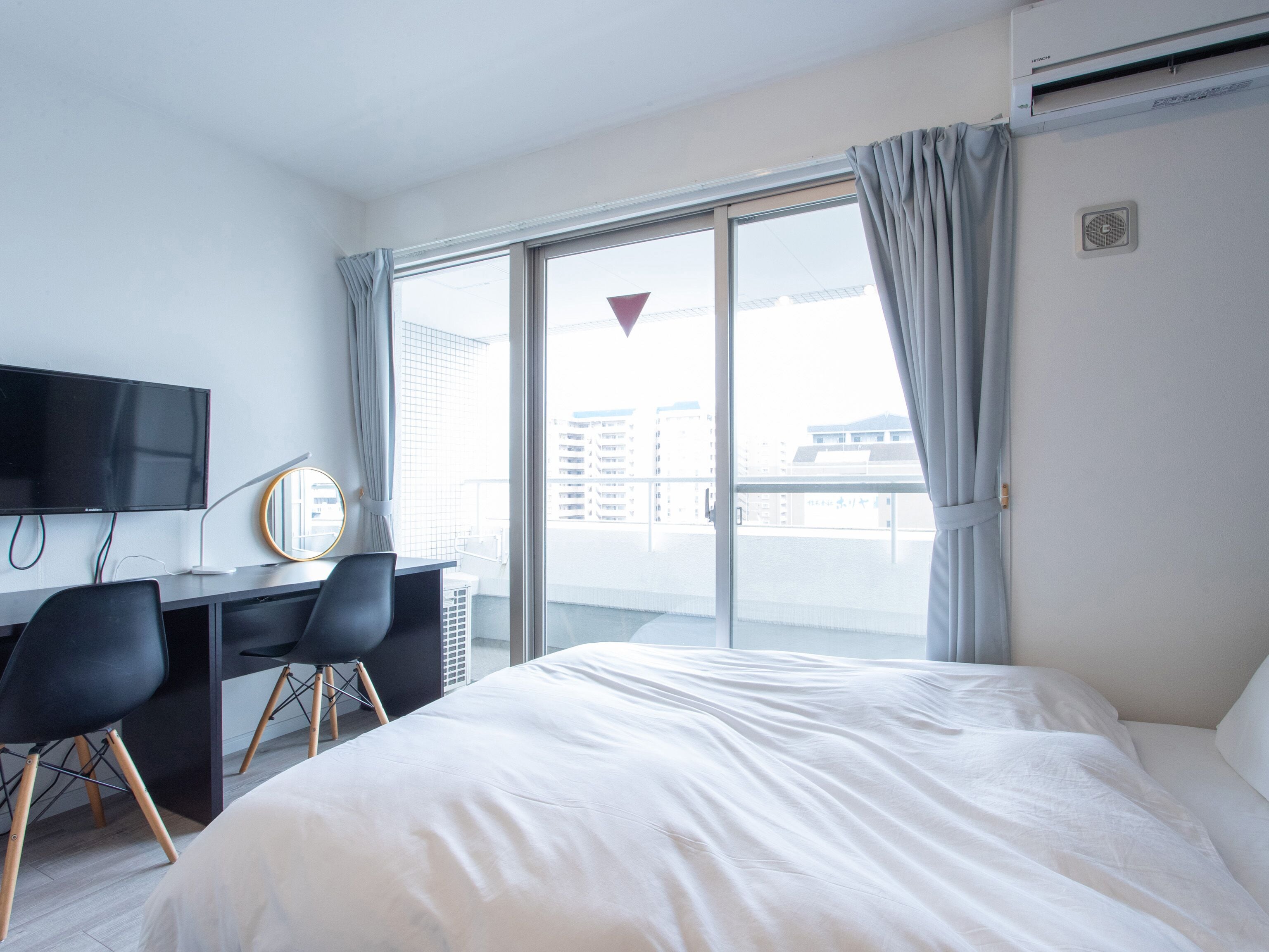 A hotel room with a bed, a desk with a computer, a TV, and a large window with curtains.